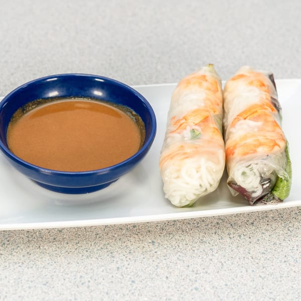 Two fresh Vietnamese spring rolls with shrimp and noodles, served with a side of peanut sauce.