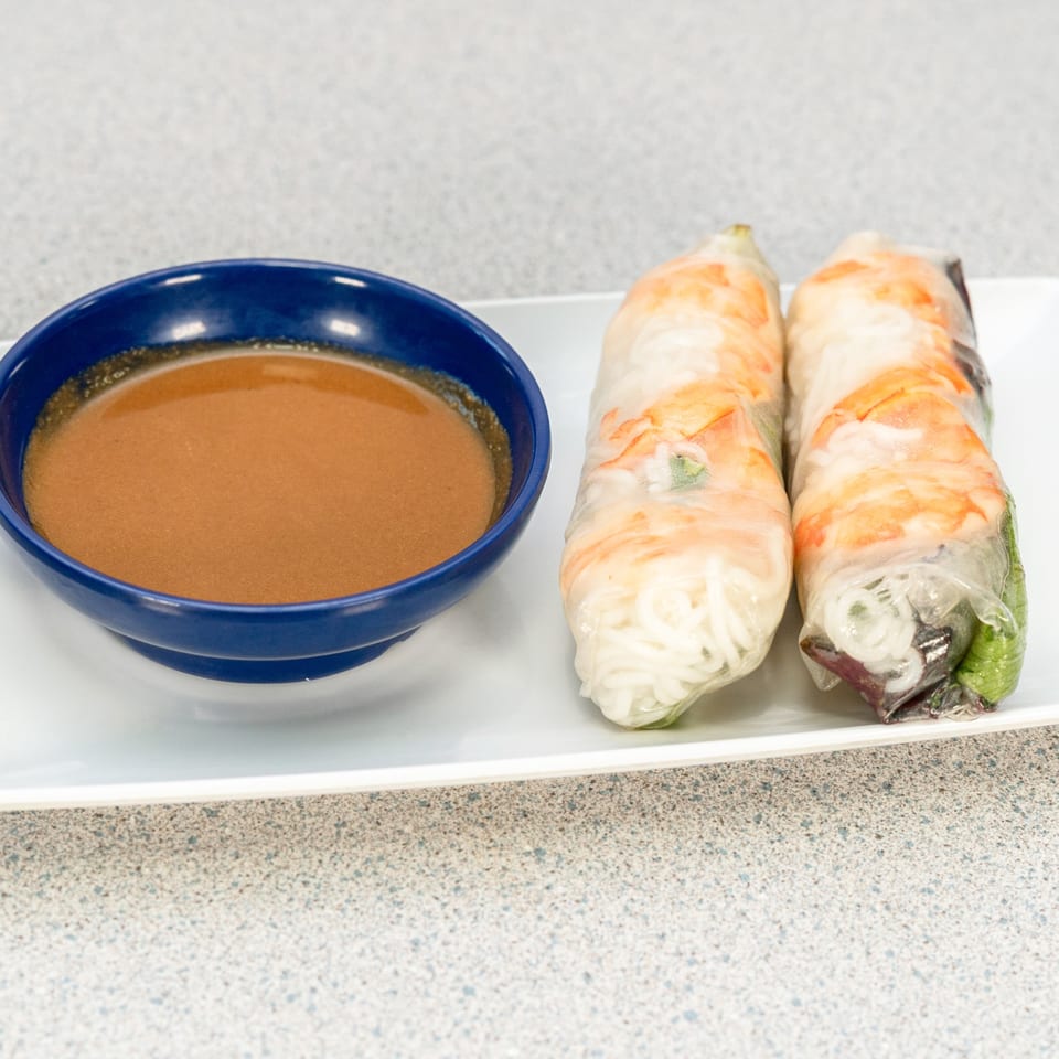 Two fresh Vietnamese spring rolls with shrimp and noodles, served with a side of peanut sauce.