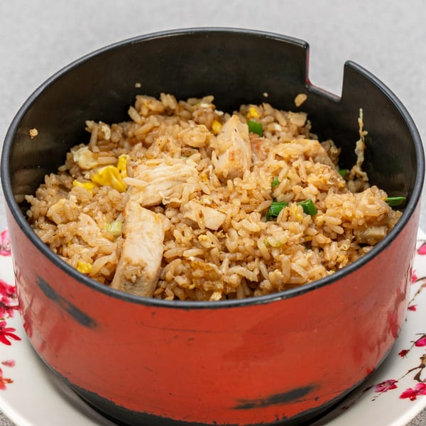 Chicken fried rice with green onions and scrambled egg in a red and black bowl.
