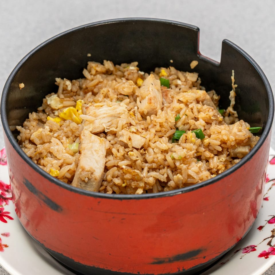 Chicken fried rice with green onions and scrambled egg in a red and black bowl.