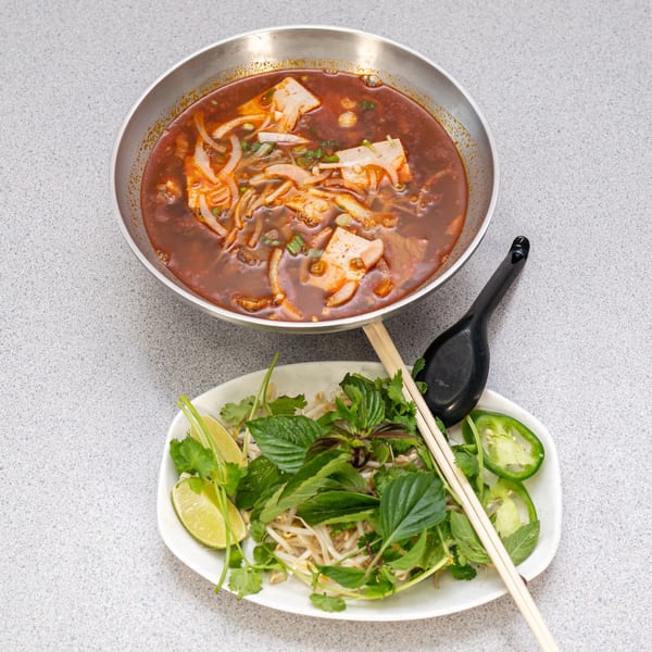 Spicy Vietnamese Bun Bo Hue soup with a side plate of fresh herbs, lime, and jalapeños.