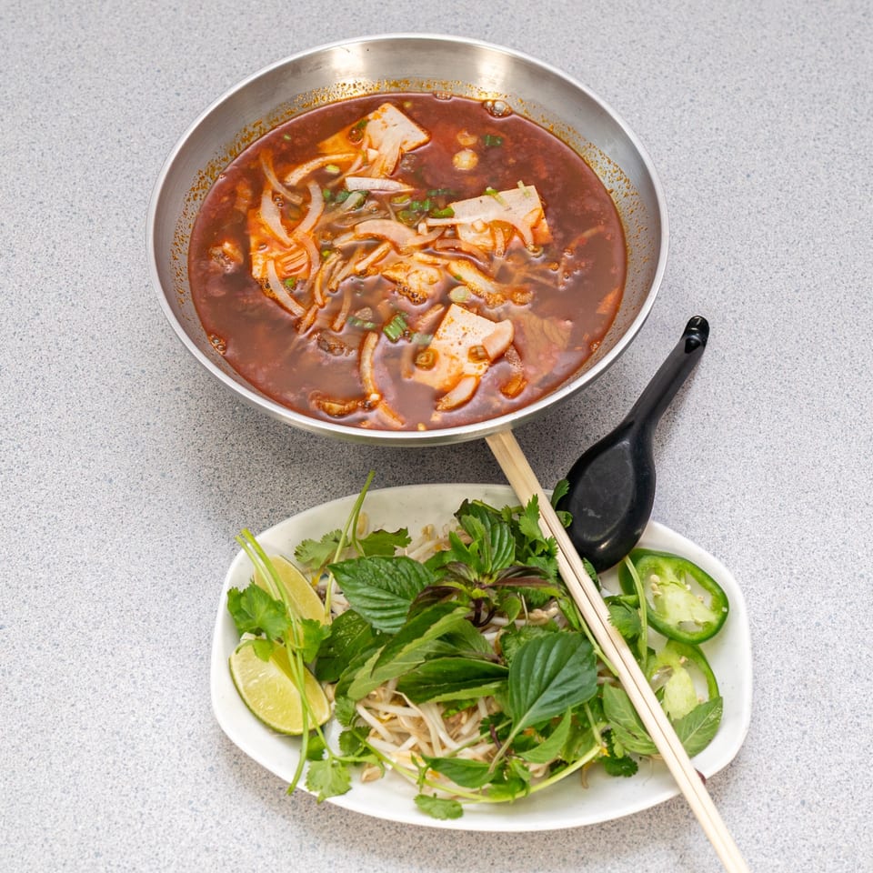 Spicy Vietnamese Bun Bo Hue soup with a side plate of fresh herbs, lime, and jalapeños.