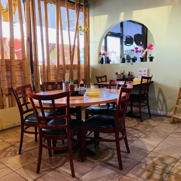 Interior of Saigon Bay restaurant with wooden tables, chairs, bamboo window coverings, and an arched window.