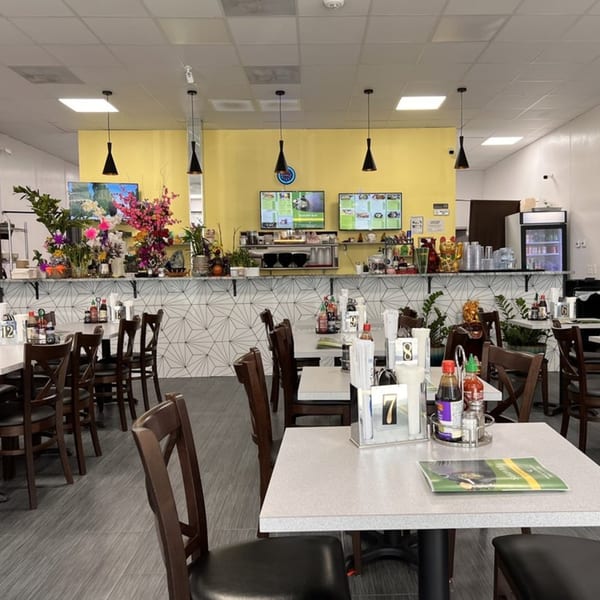 Interior of Saigon Bay restaurant with yellow walls, dark wood chairs, and white tables with condiments.