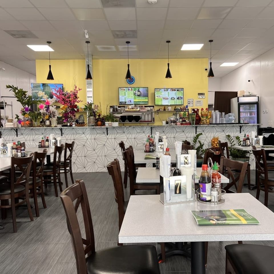 Interior of Saigon Bay restaurant with yellow walls, dark wood chairs, and white tables with condiments.