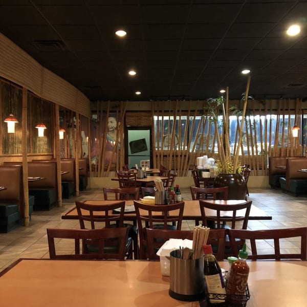 Interior of Saigon Bay restaurant with bamboo decor, booths, and tables set with chopsticks and condiments.