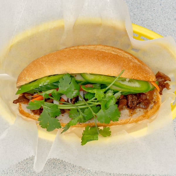 A Saigon Bay banh mi sandwich with meat, cilantro, and green peppers in a yellow basket.