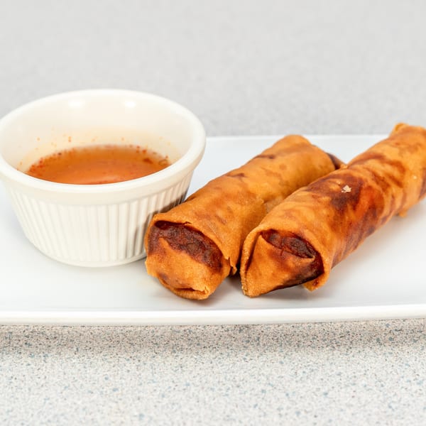 Two crispy Vietnamese egg rolls with a side of sweet chili dipping sauce on a white plate.