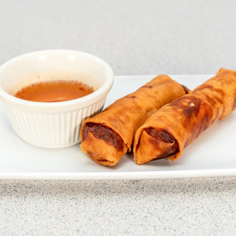Two crispy Vietnamese egg rolls with a side of sweet chili dipping sauce on a white plate.