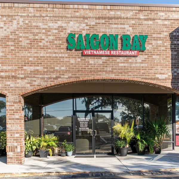 Exterior of Saigon Bay Vietnamese Restaurant with a brick facade, green sign, and potted plants.