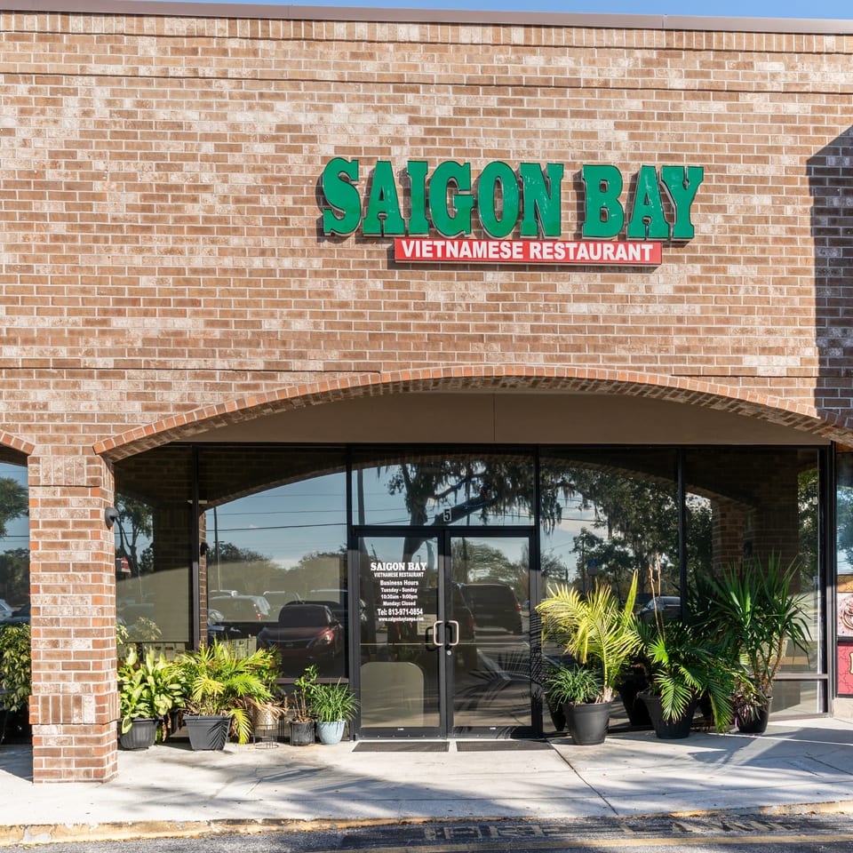 Exterior of Saigon Bay Vietnamese Restaurant with a brick facade, green sign, and potted plants.