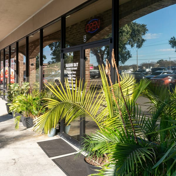 Exterior of Saigon Bay Vietnamese Restaurant with potted plants and an "OPEN" sign in the window.
