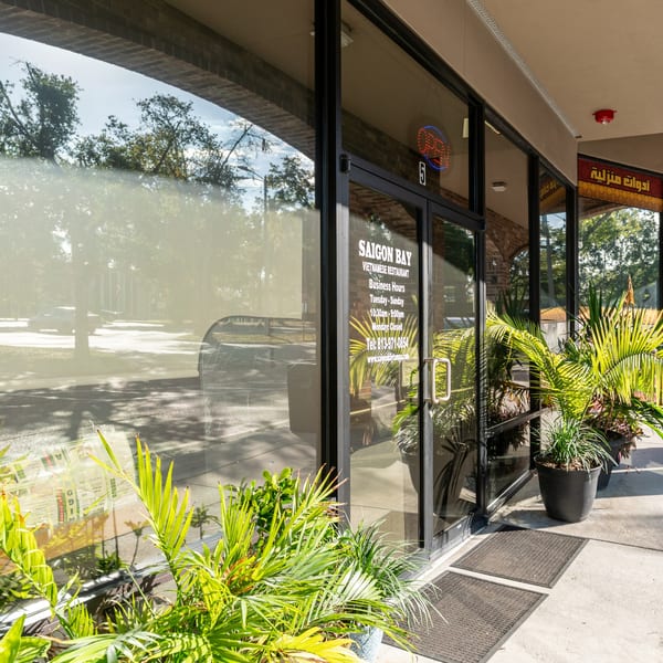 Exterior of Saigon Bay Vietnamese Restaurant with business hours on the glass door, surrounded by potted plants.