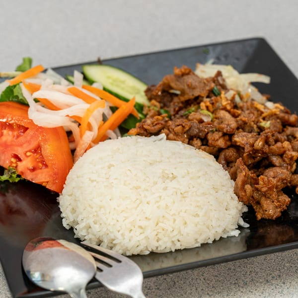 Vietnamese dish with white rice, stir-fried meat, sliced tomatoes, cucumbers, and pickled vegetables.